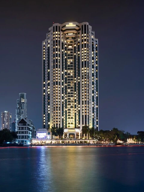 The Peninsula Bangkok tower lit up over the river at night